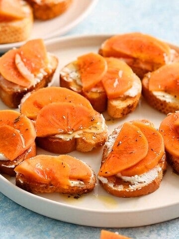 crostinis topped with persimmon in a white plate.