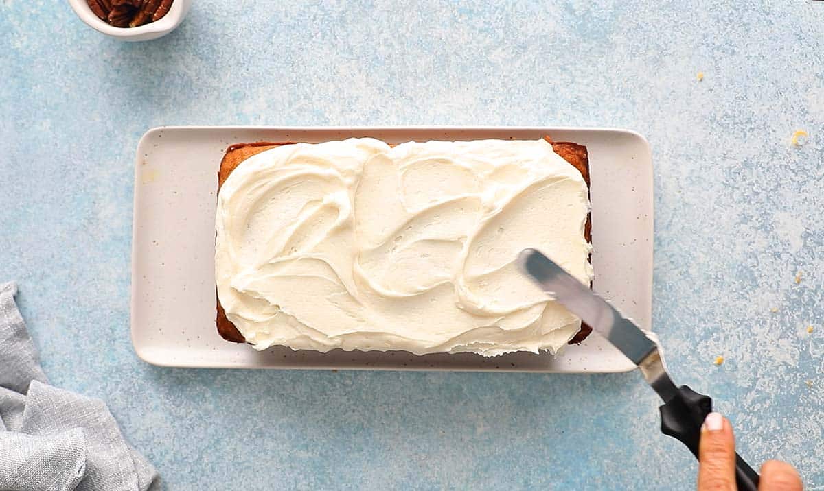 a hand spreading white frosting on a loaf cake.