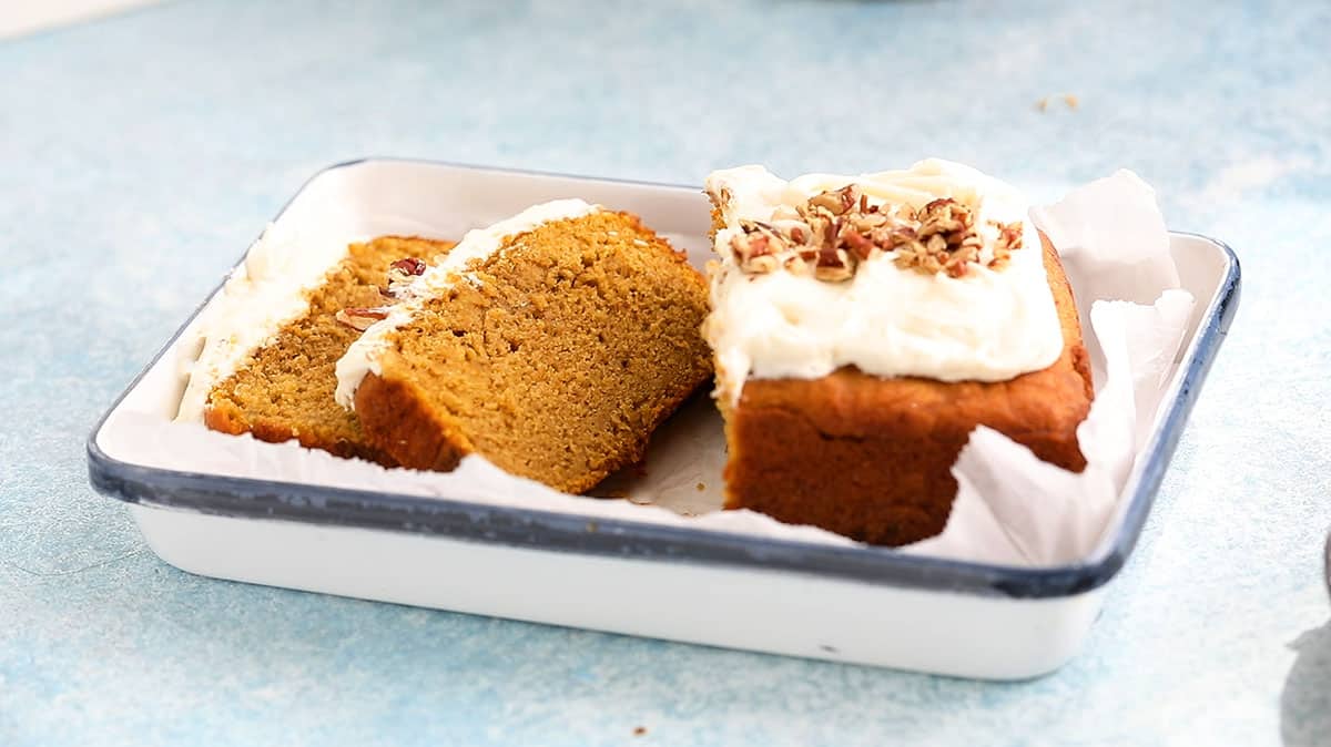 sliced pumpkin cake topped with chopped pecans on a white tray. 