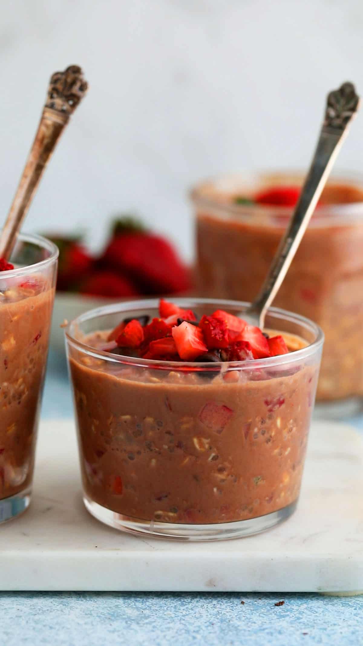 two glass jars with brown oats topped with chopped strawberries.
