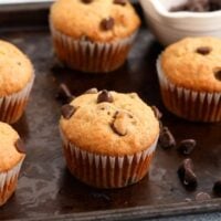 5 banana chocolate chip muffins placed on a black metal tray.