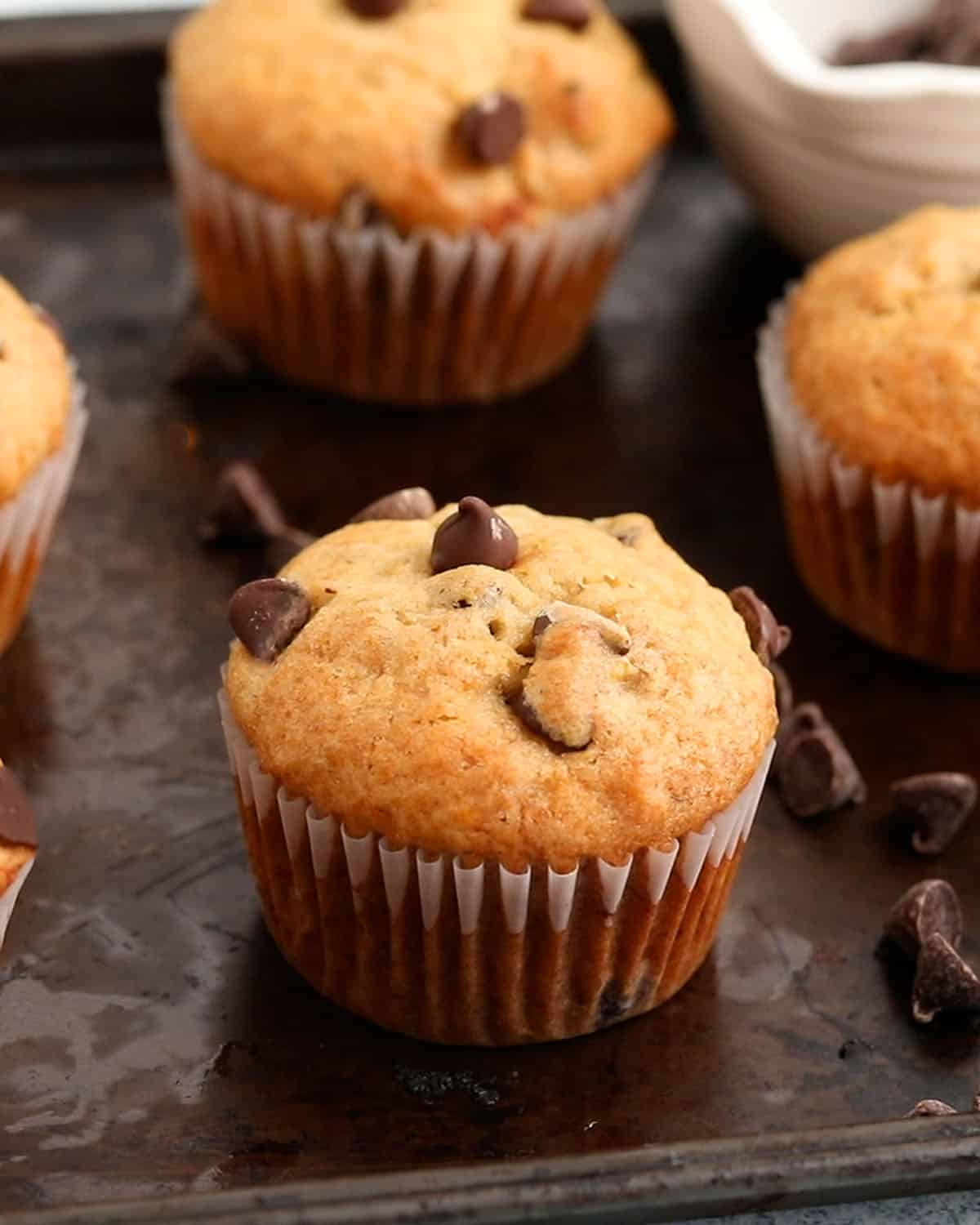 5 banana chocolate chip muffins placed on a black metal tray.