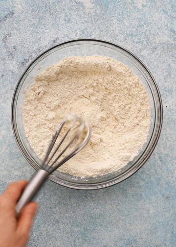 a hand whisking flour in a glass bowl.