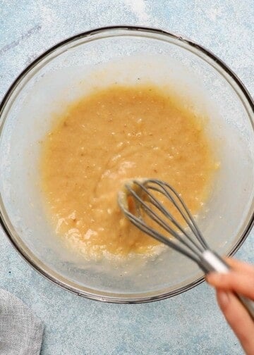 a hand whisking wet batter in a glass bowl.