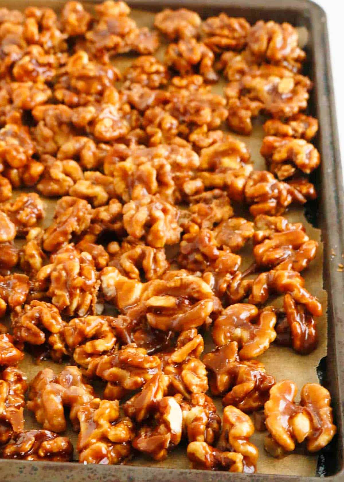 grey metal baking sheet with caramel walnuts.