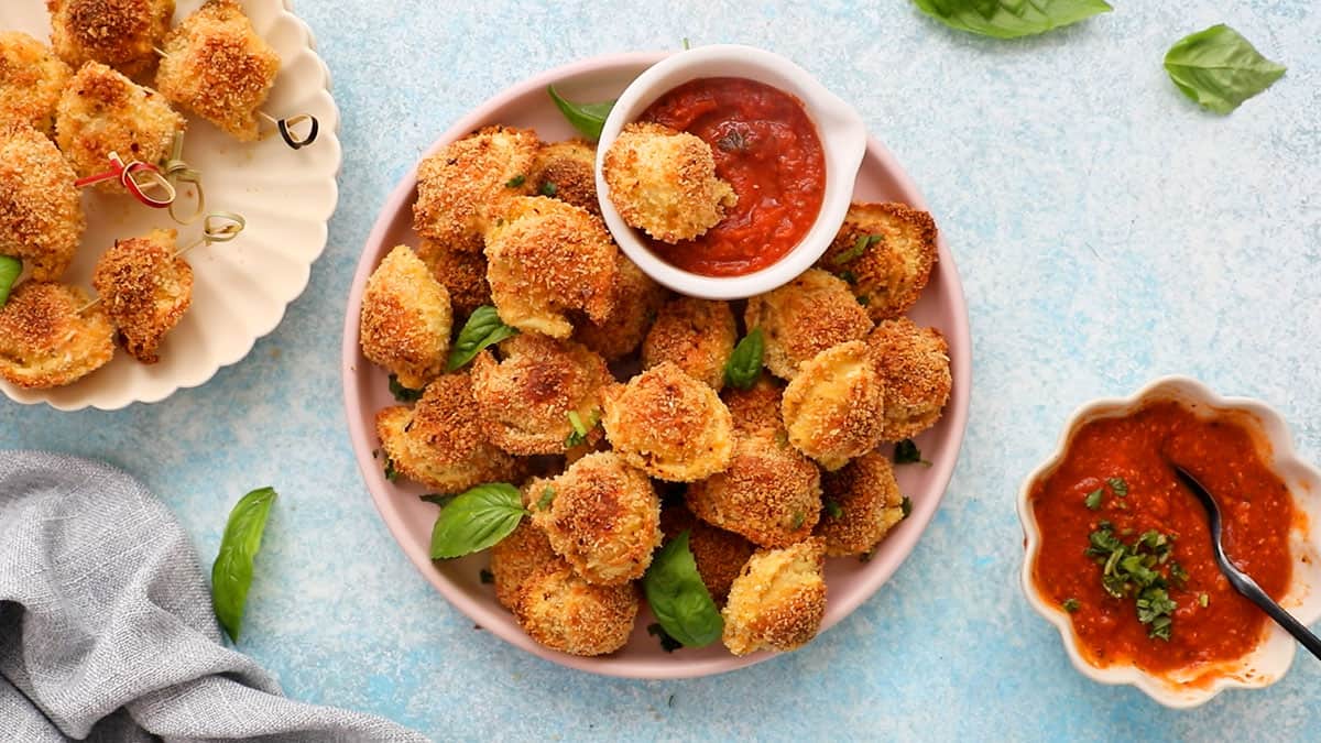 golden breaded tortellini bites in a pink round plate along with red sauce in a white bowl.