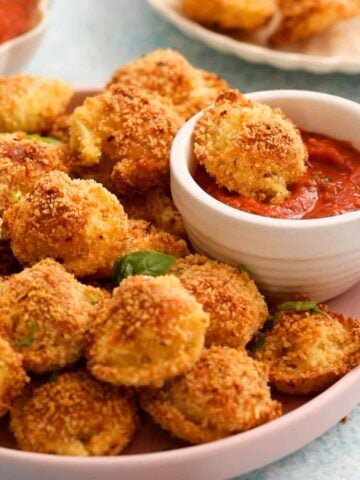 golden brown breaded tortellini in a pink plate along with red sauce.