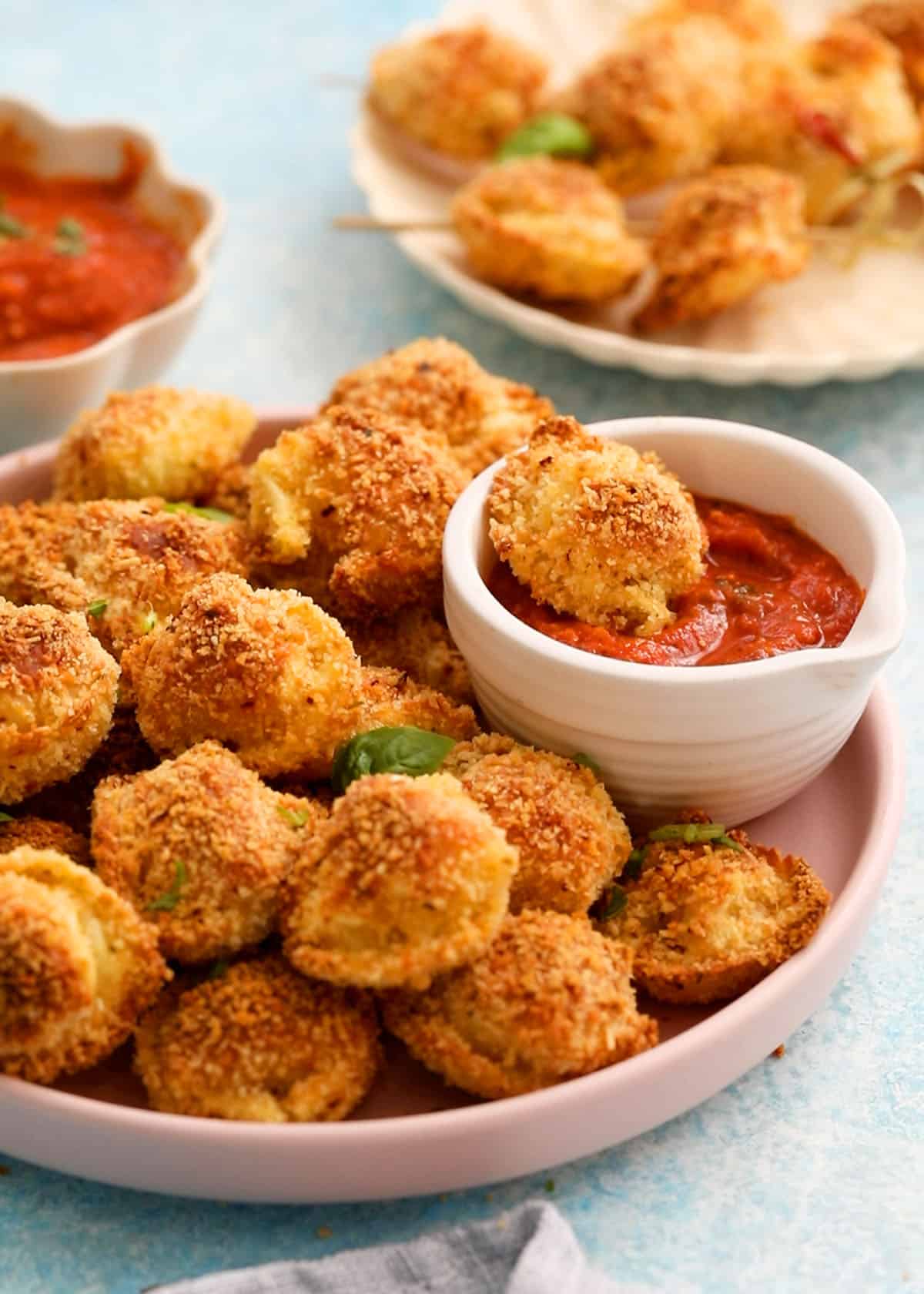 golden breaded tortellini bites in a pink round plate along with red sauce in a white bowl.