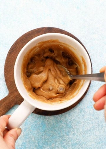 a hand mixing brown chocolate chip cake batter in a white mug.