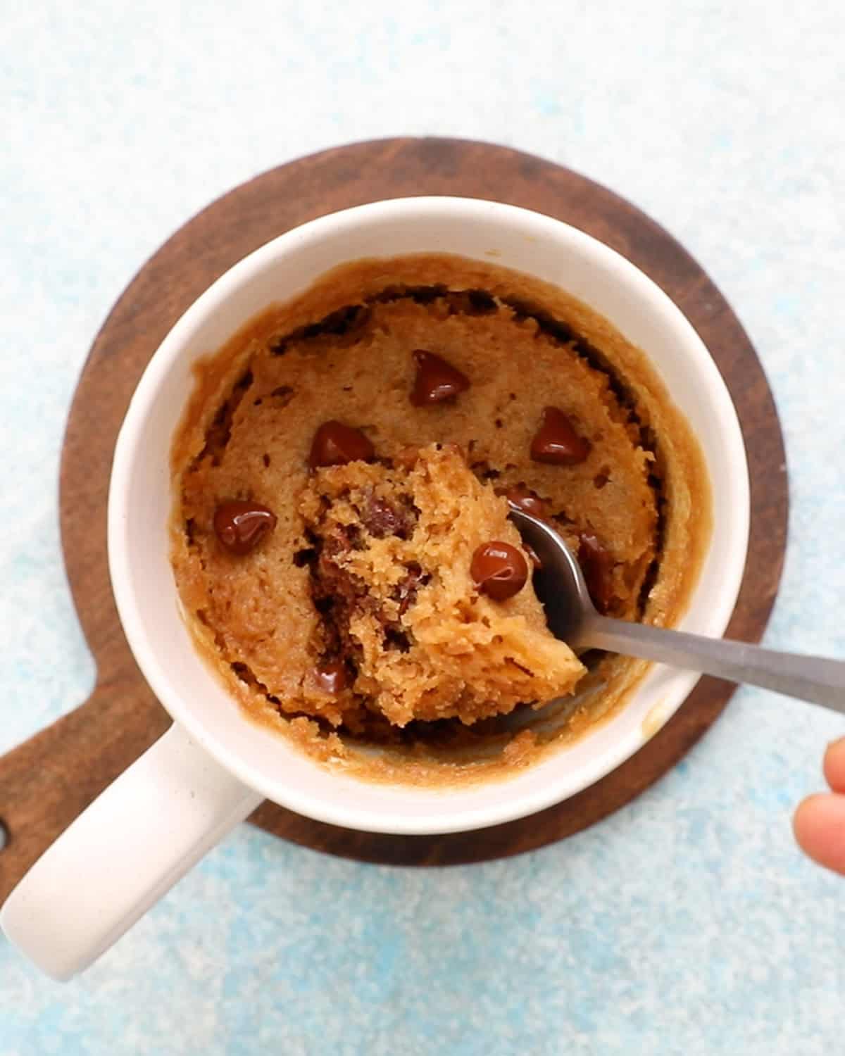 brown cake topped with chocolate chips in a white mug along with a spoon.