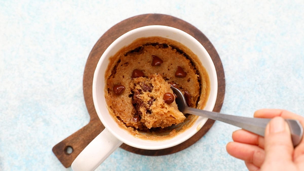 brown cake topped with chocolate chips in a white mug along with a spoon.