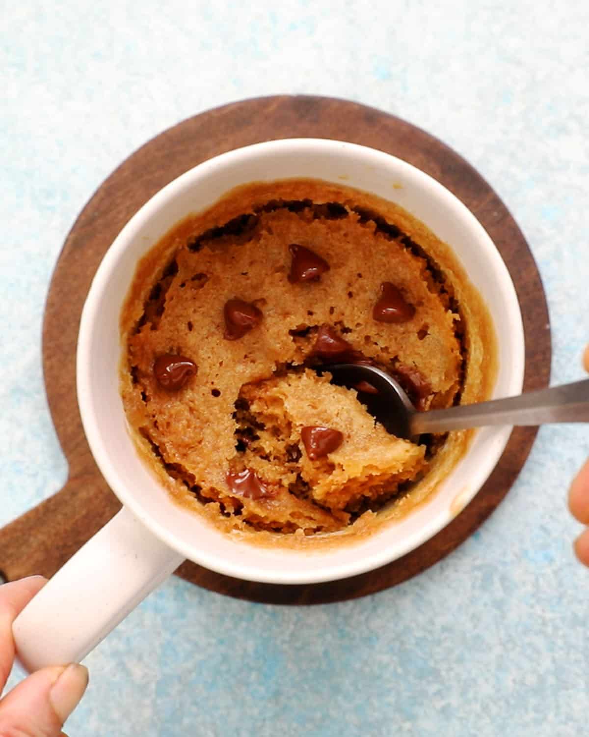 brown cake topped with chocolate chips in a white mug along with a spoon.