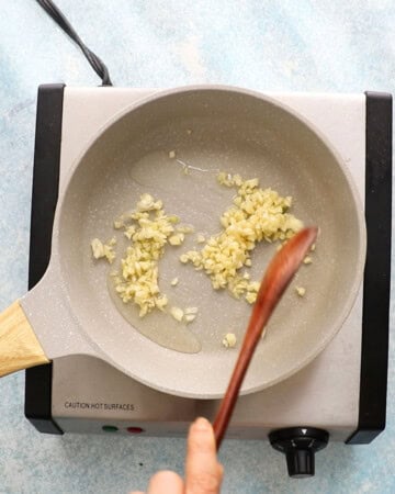 a hand cooking chopped garlic in a white skillet.