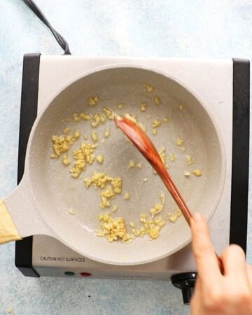 a hand cooking chopped garlic in a white skillet.