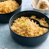 cooked garlic fried rice in two blue bowls along with a black spoon.