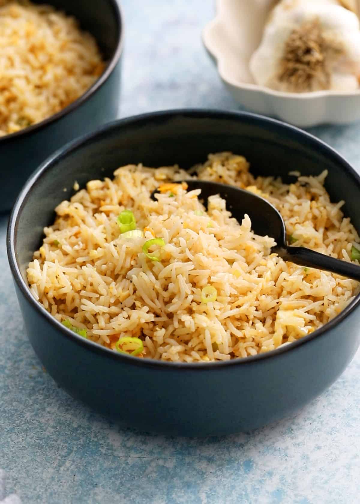 cooked garlic fried rice in two blue bowls along with a black spoon.