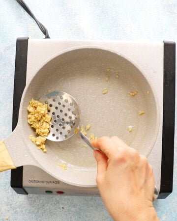 a hand cooking chopped garlic in a white skillet.