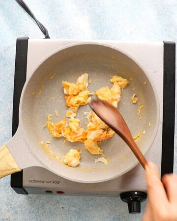a hand cooking chopped eggs in a white skillet.