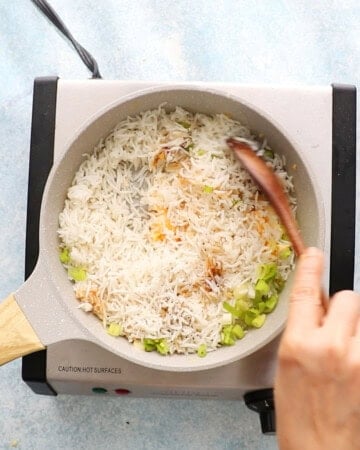 a hand stir frying fried rice in a white skillet.