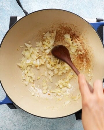 a hand sauteing chopped onion in a white pan.