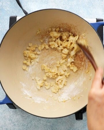 a hand sauteing chopped onion in a white pan.