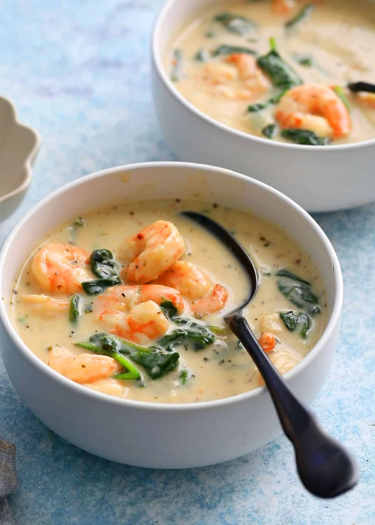 shrimp and spinach soup in a white bowl along with a black spoon.