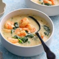 shrimp and spinach soup in a white bowl along with a black spoon.