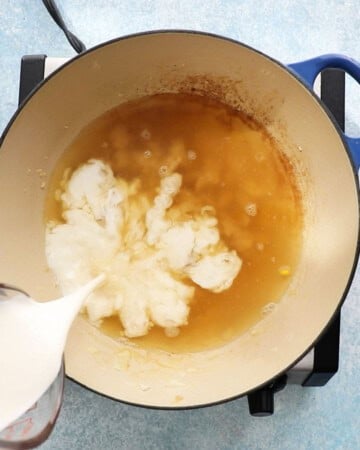 a hand pouring white milk into a pan with stock.