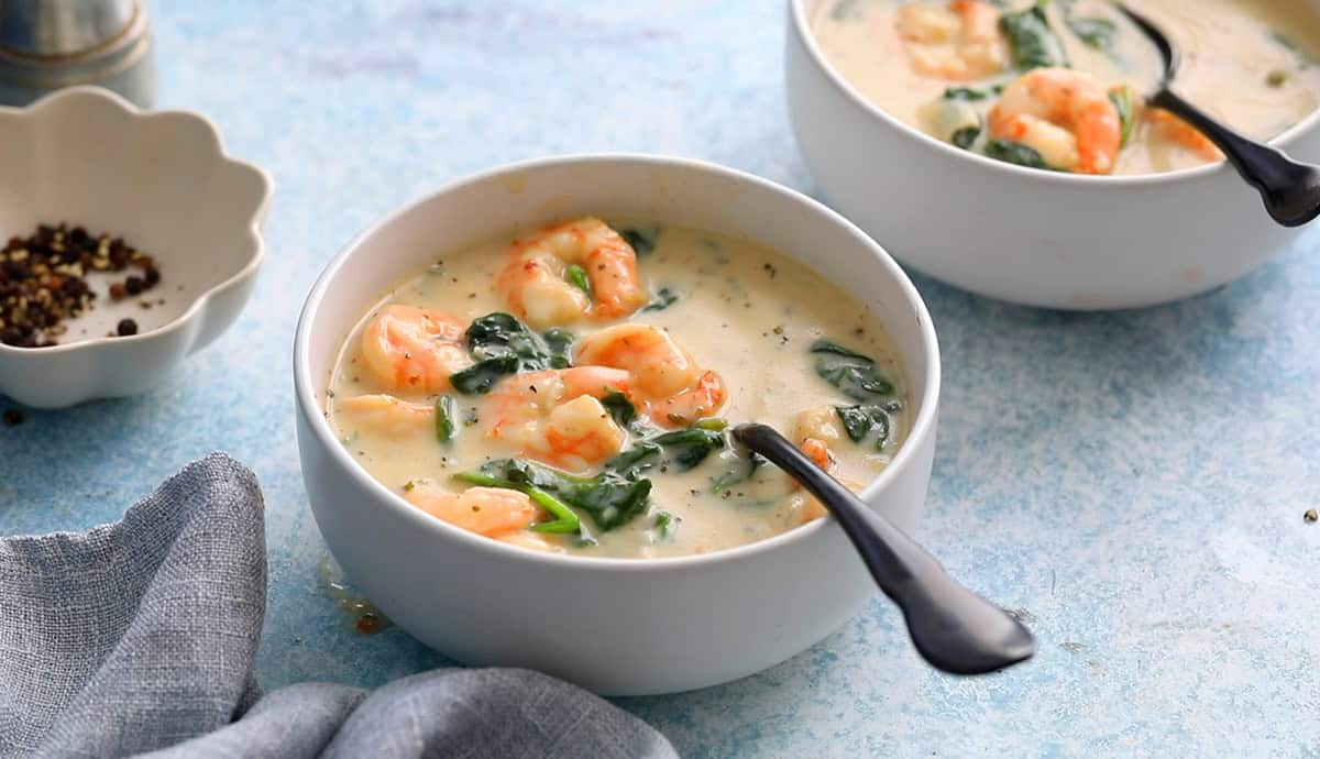 shrimp and spinach soup in a white bowl along with a black spoon.