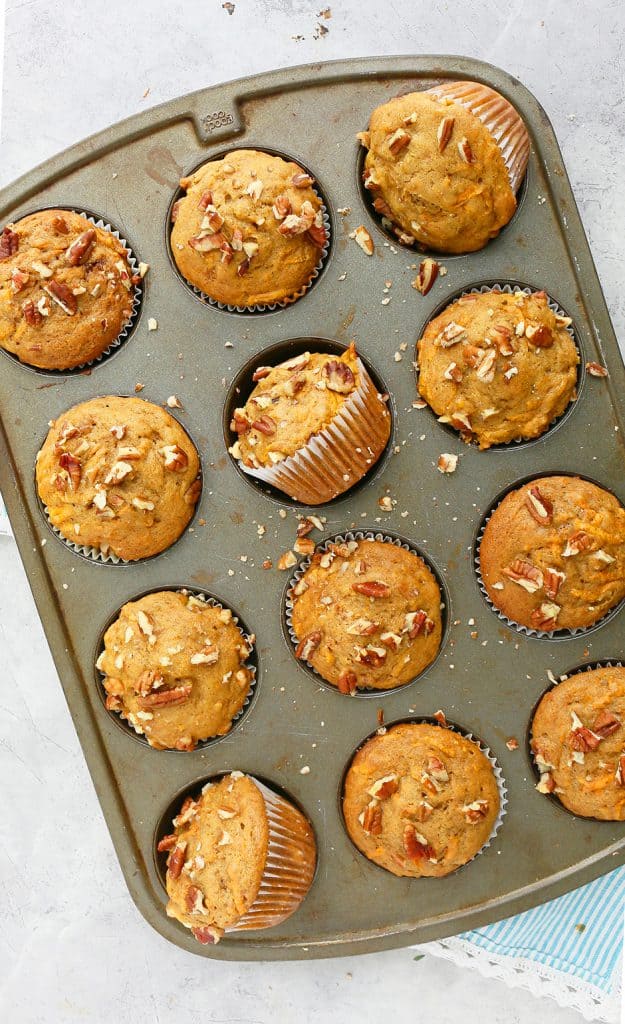 A 12 cup muffin pan with freshly baked sweet potato muffins topped with chopped pecans