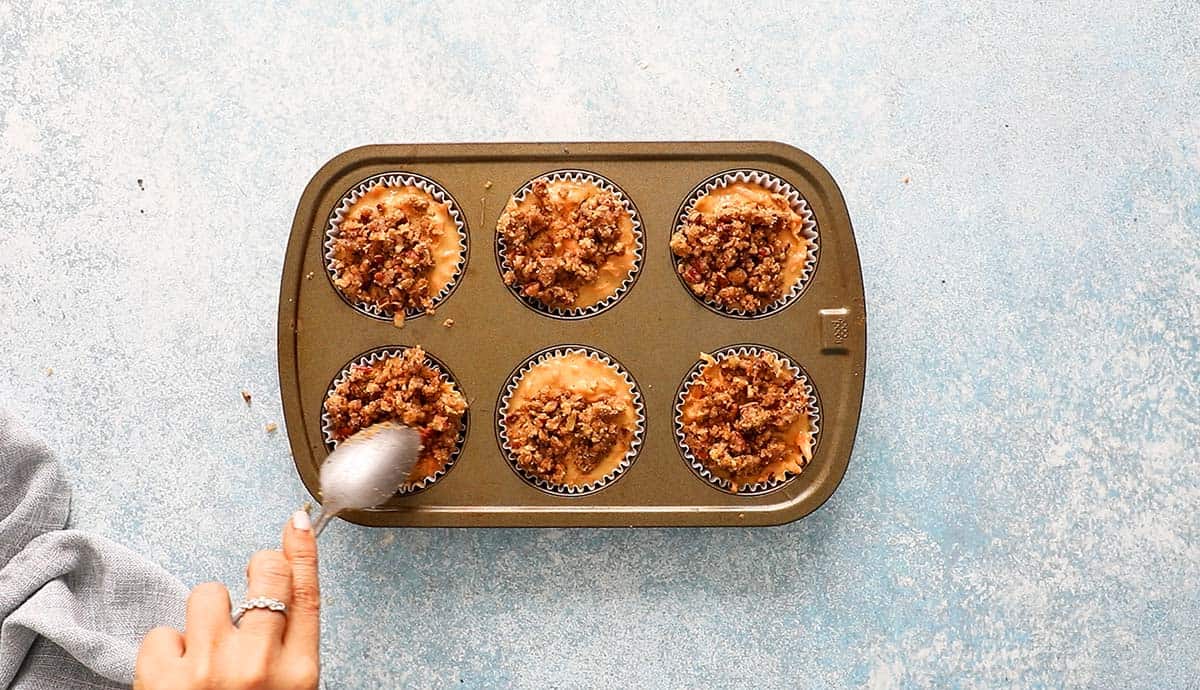 a hand adding topping on top of muffin batter using a spoon.