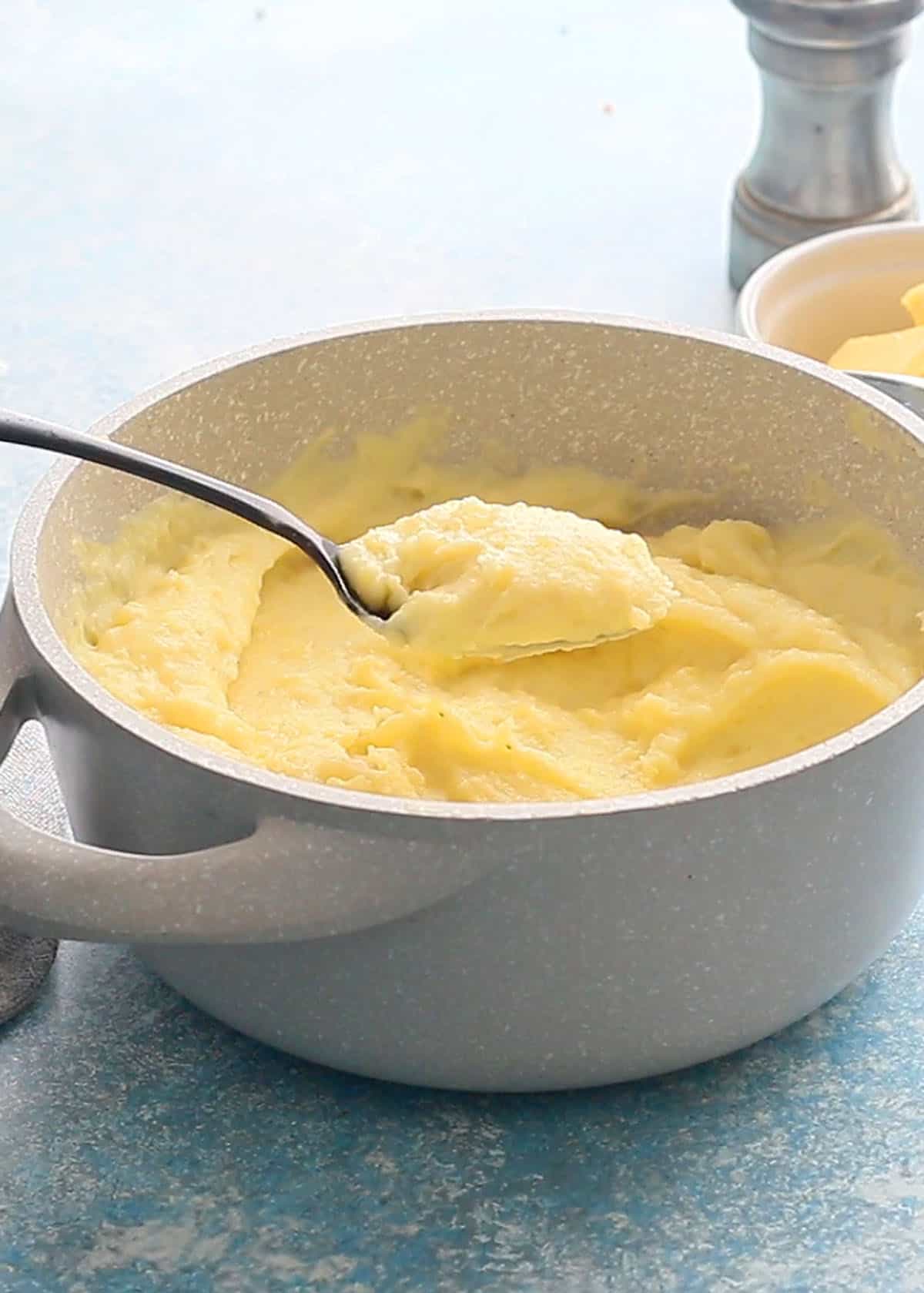 a black spoon with mashed potatoes being lift from a white pot.