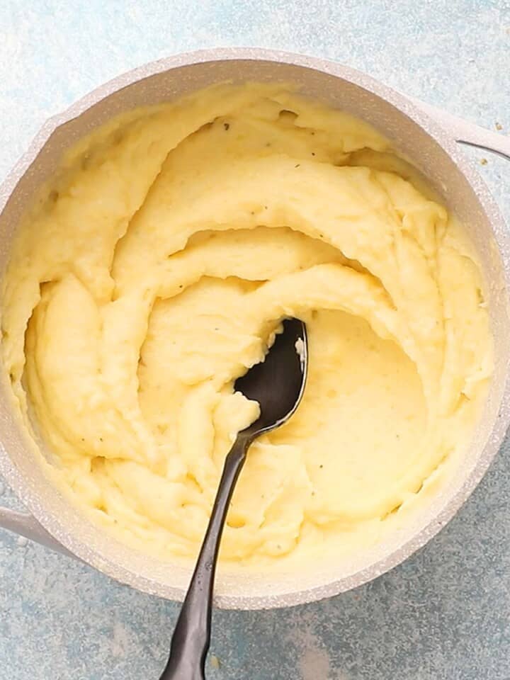 a white pot with mashed potatoes along with a black spoon.