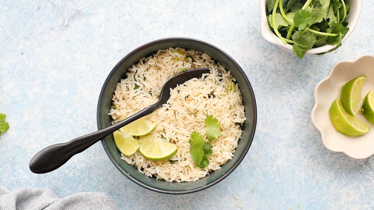 cooked cilantro lime rice in a blue bowl along with a black spoon.