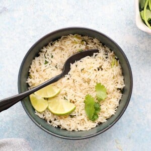 cooked cilantro lime rice in a blue bowl along with a black spoon.