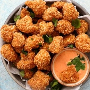 Golden cauliflower nuggets in a round pan along with a bowl of pink sauce.