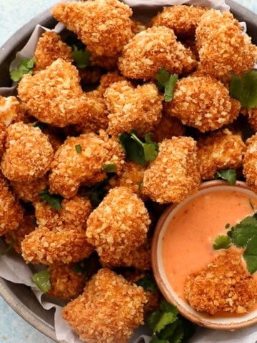 Golden cauliflower nuggets in a round pan along with a bowl of pink sauce.