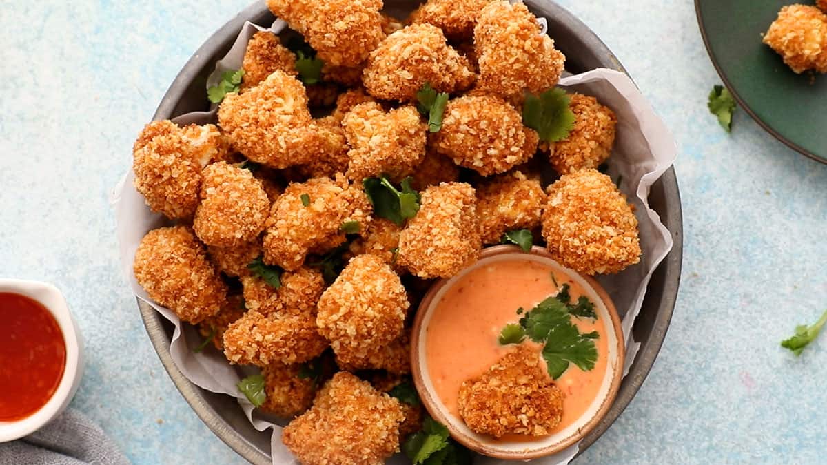 Golden cauliflower nuggets in a round pan along with a bowl of pink sauce.
