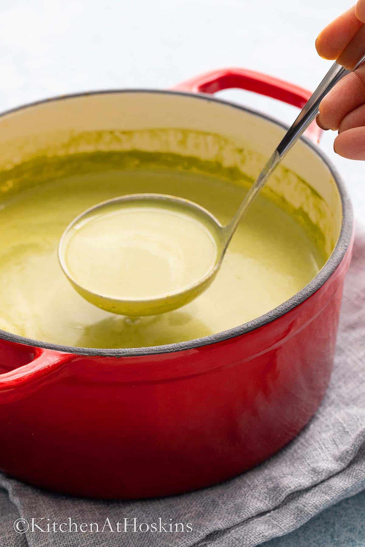 red pot with creamy spinach soup being served with a ladle.