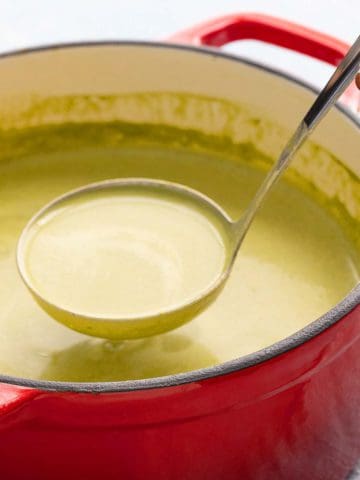 lifting a ladle with spinach soup from a red pot with the same.