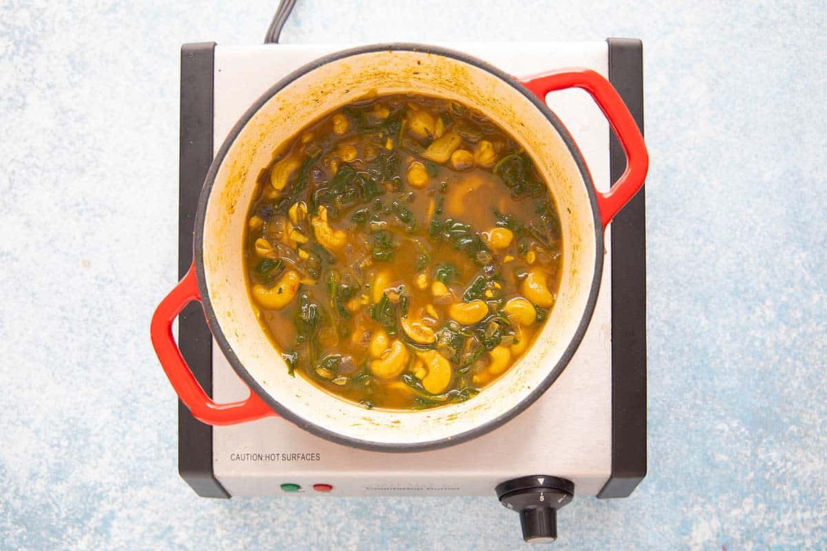 a pot with simmering spinach and cashew soup on a stove top.