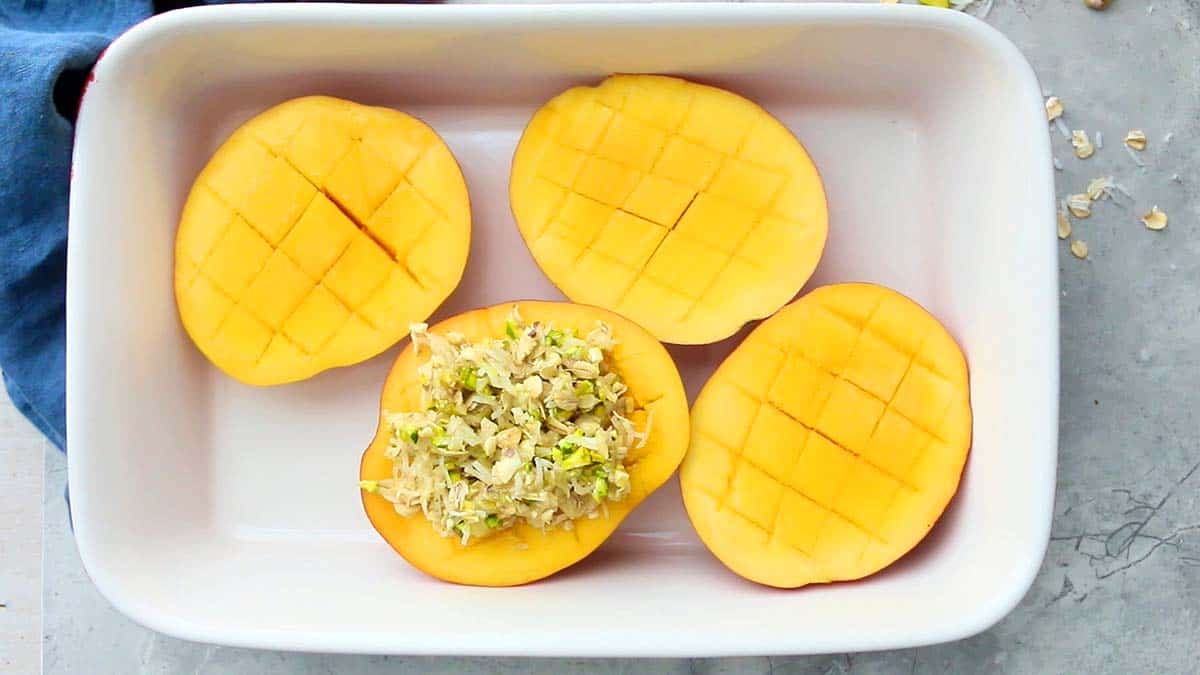 4 cut mango halves in a white rectangle dish.