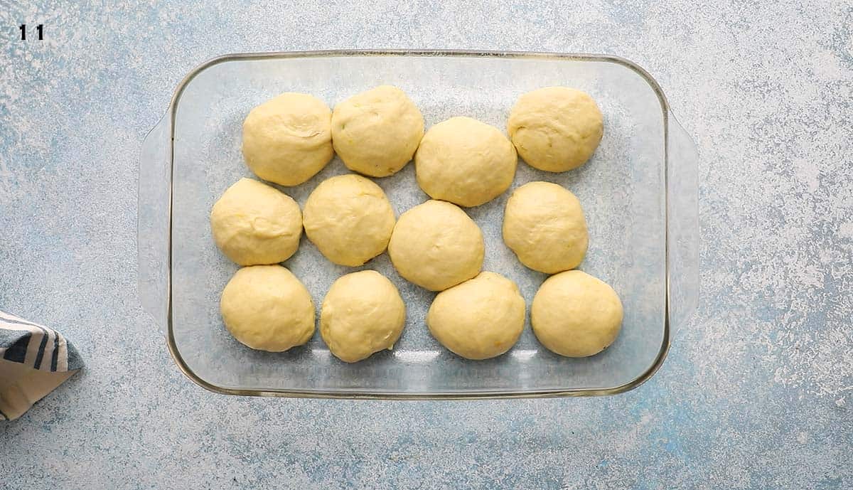 12 yeast dough balls placed in a rectangular glass dish.