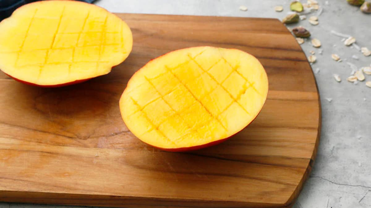 two cut mango halves on a wooden cutting board.