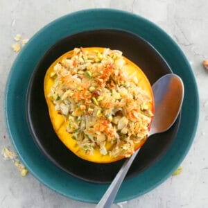 one baked mango half on two plates along with a spoon.