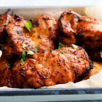 cooked orange chicken thighs in a white platter garnished with green cilantro.