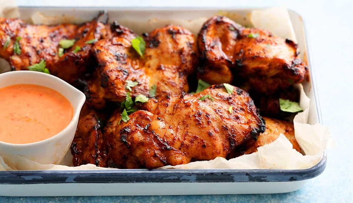 cooked orange chicken thighs in a white platter garnished with green cilantro.