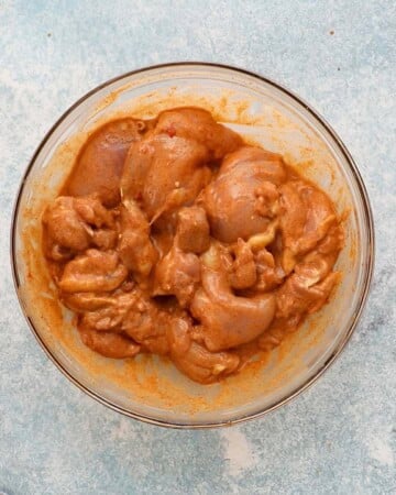 marinated orange chicken thighs in a large glass bowl.