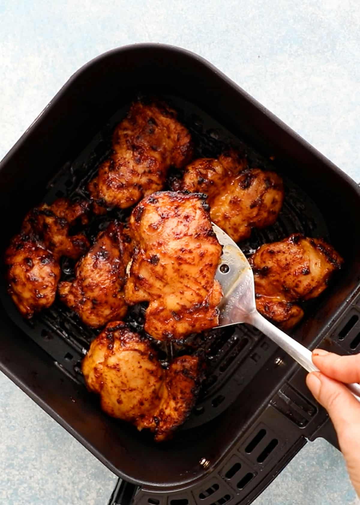 a hand holding one cooked orange colored chicken thigh using a flat spatula.