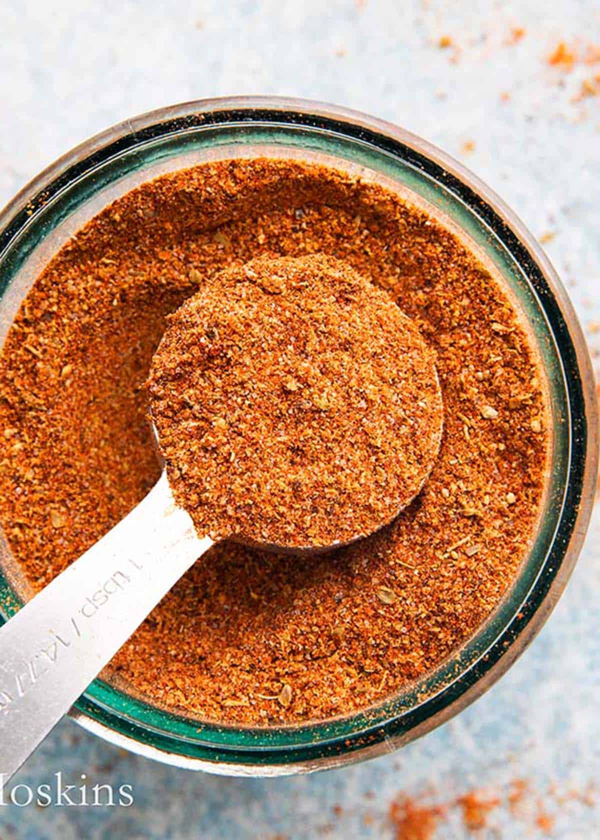 red colored ground spices in a glass jar along with a tablespoon.